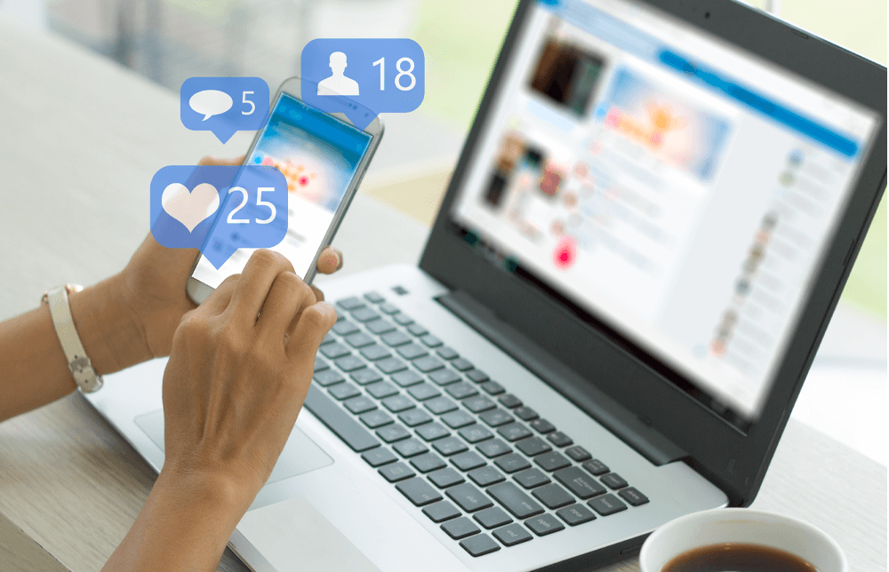 A woman holding her mobile while Facebook is blurred on her PC, hinting she's using the app A woman holding her mobile while Facebook is blurred on her PC, hinting she's using the app